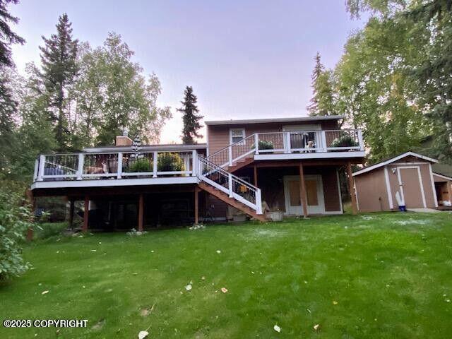 rear view of property with a shed, a deck, a lawn, and an outdoor structure