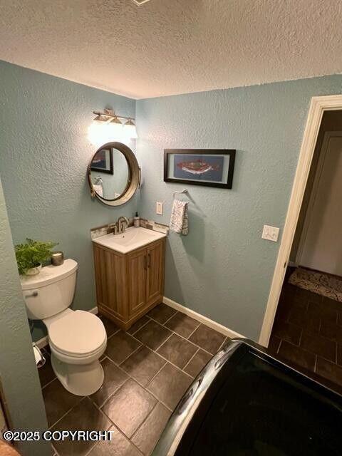 bathroom with a textured ceiling, tile patterned flooring, toilet, a textured wall, and vanity
