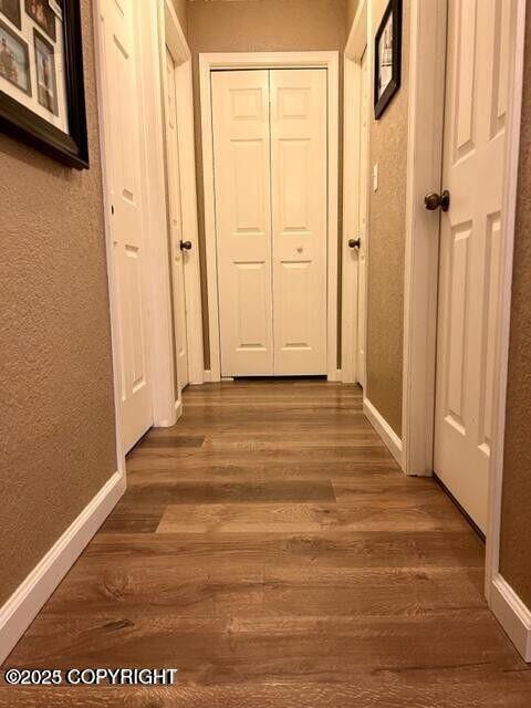 hallway with baseboards, wood finished floors, and a textured wall