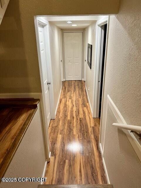 corridor featuring light wood-style flooring, a textured wall, and baseboards