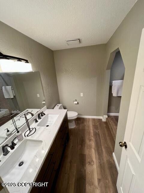bathroom with a textured ceiling, wood finished floors, toilet, double vanity, and a textured wall