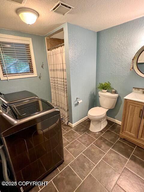 full bath featuring a textured ceiling, tile patterned flooring, a shower with shower curtain, toilet, and washer / dryer