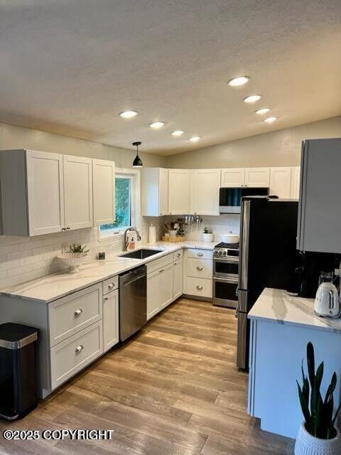 kitchen featuring appliances with stainless steel finishes, a sink, backsplash, light wood-style floors, and recessed lighting