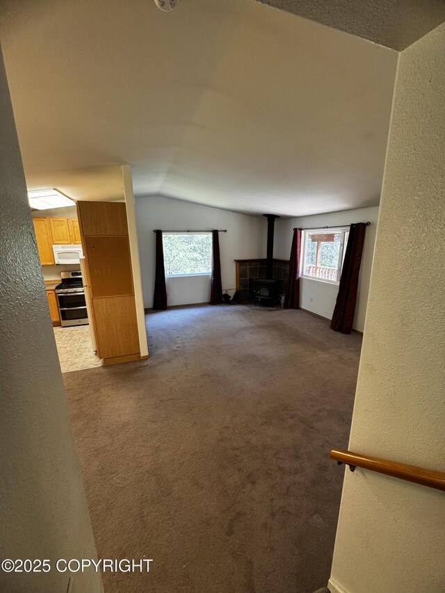 33325 Vinewood Ln, Seward, AK 99664 - unfurnished living room with a textured wall, a wood stove, lofted ceiling, healthy amount of natural light, and carpet