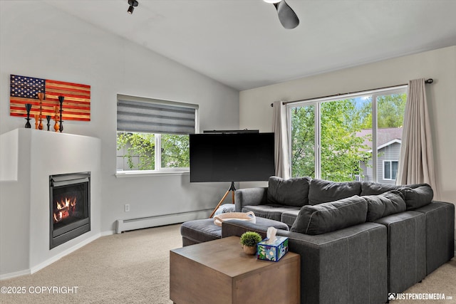 living room with a baseboard radiator, carpet flooring, vaulted ceiling, a warm lit fireplace, and plenty of natural light