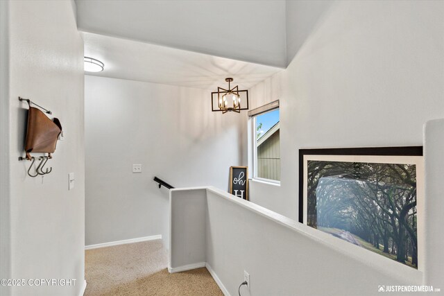 hallway with an upstairs landing, carpet, a chandelier, and baseboards