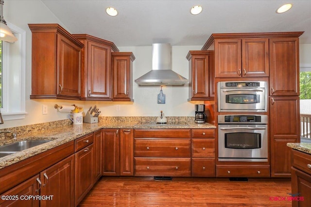 2750 E Whispering Woods Dr, Wasilla, AK 99654 - kitchen with wall chimney range hood, stainless steel double oven, black electric stovetop, wood finished floors, and light stone counters