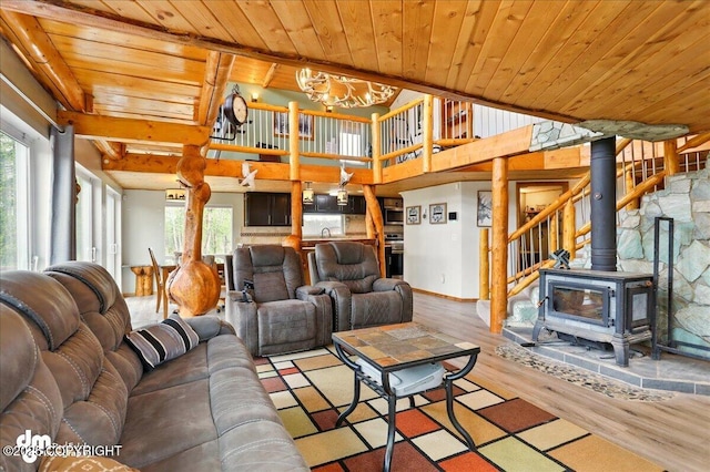 living room with wood finished floors, healthy amount of natural light, wooden ceiling, a wood stove, and a chandelier