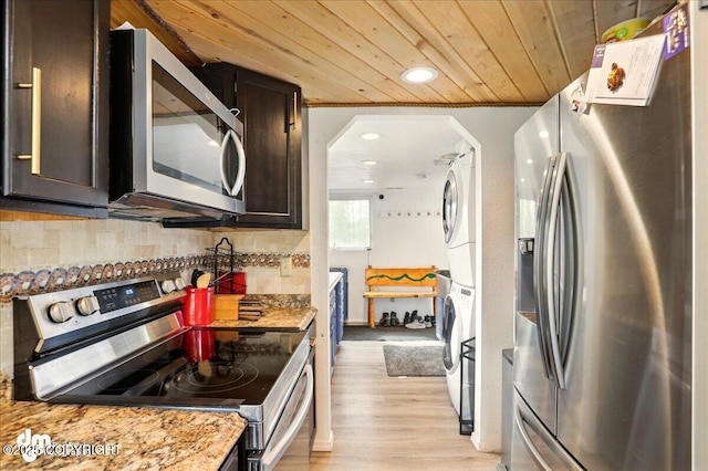 kitchen with appliances with stainless steel finishes, stacked washer / dryer, wood ceiling, backsplash, and dark brown cabinetry
