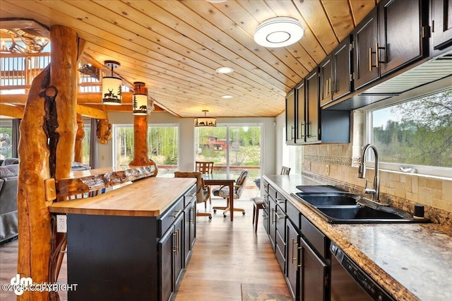 kitchen featuring butcher block countertops, a sink, light wood finished floors, backsplash, and decorative light fixtures