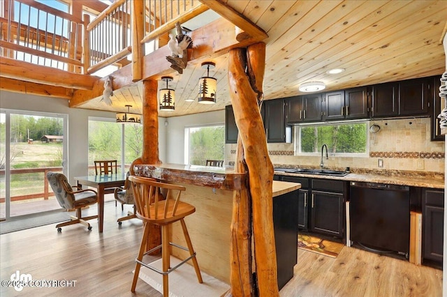 kitchen featuring a sink, dishwasher, light wood finished floors, tasteful backsplash, and a breakfast bar