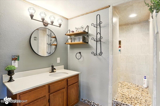 bathroom with walk in shower, vanity, and a textured wall