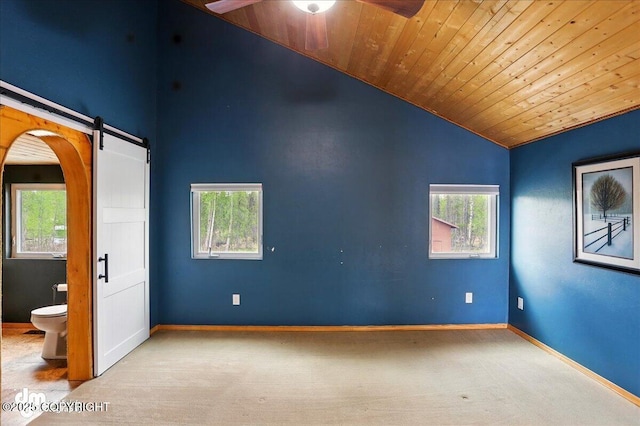 empty room featuring vaulted ceiling, carpet floors, a barn door, wooden ceiling, and ceiling fan