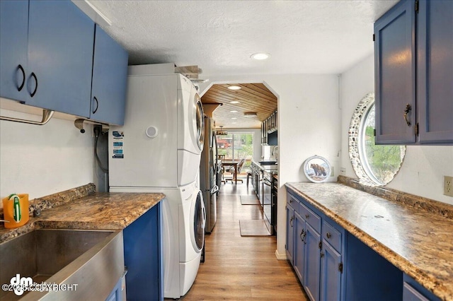 kitchen featuring blue cabinetry, stacked washer / dryer, light wood finished floors, recessed lighting, and a sink