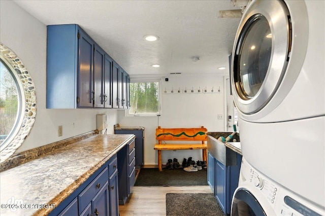 laundry area with stacked washing machine and dryer, light wood-style flooring, recessed lighting, and cabinet space