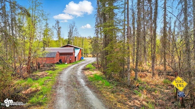 view of dirt / gravel road with a barn and a view of trees