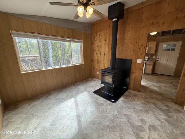 26155 W Long Lake Rd, Willow, AK 99688 - unfurnished living room featuring wooden walls, a wood stove, a ceiling fan, and stone finish flooring