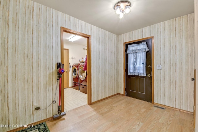 foyer entrance featuring washer and dryer, wood finished floors, wallpapered walls, and baseboards