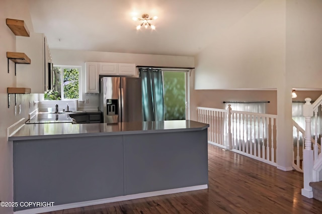 kitchen with stainless steel refrigerator with ice dispenser, a peninsula, dark wood-type flooring, white cabinets, and a sink