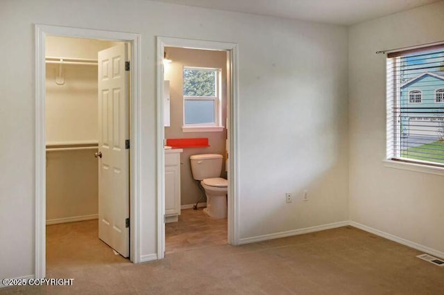 unfurnished bedroom featuring a walk in closet, a closet, and light carpet