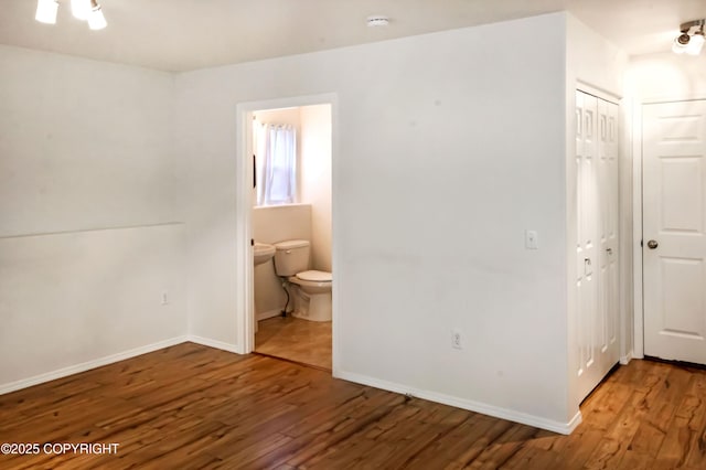 unfurnished bedroom with wood-type flooring, ensuite bath, baseboards, and a closet