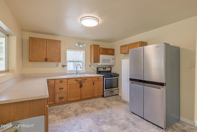 kitchen featuring appliances with stainless steel finishes, a sink, stone finish flooring, light countertops, and brown cabinetry