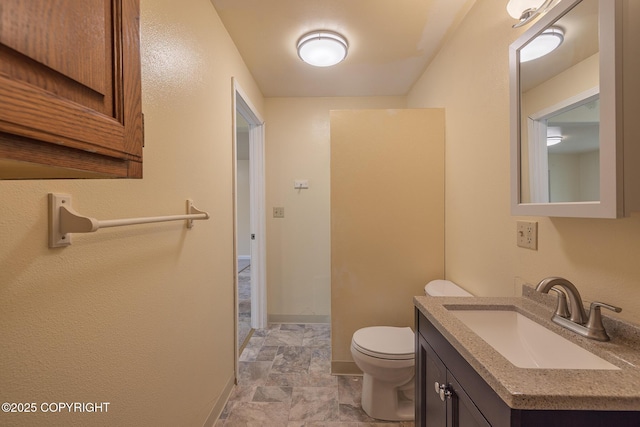 bathroom with stone finish floors, toilet, baseboards, and vanity
