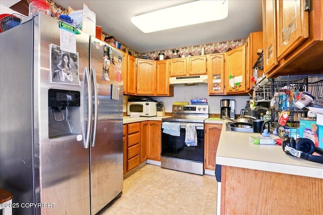 kitchen with stainless steel appliances, under cabinet range hood, light countertops, brown cabinets, and light flooring
