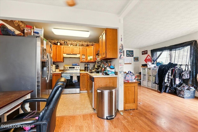 kitchen featuring stainless steel appliances, under cabinet range hood, light wood-style flooring, brown cabinetry, and a textured ceiling