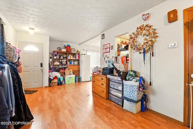 interior space with light wood finished floors, a textured ceiling, and baseboards