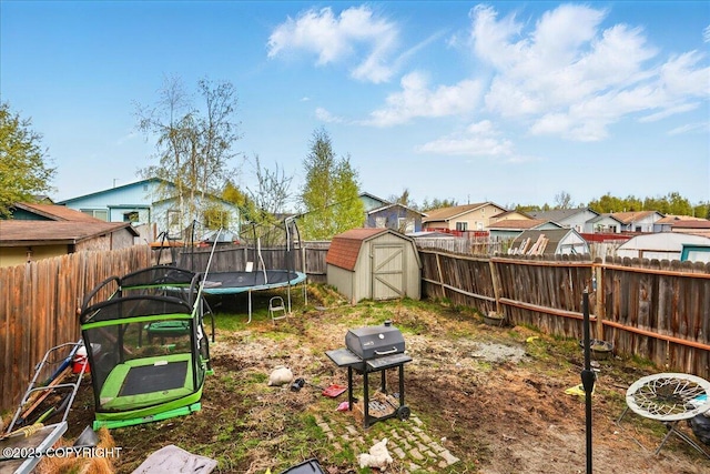 fenced backyard featuring a trampoline, a storage unit, a residential view, and an outbuilding