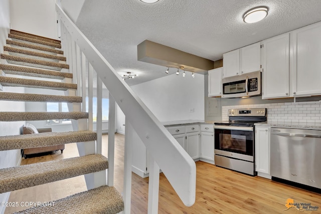832 O Pl Unit 832, Anchorage, AK 99501 - kitchen featuring appliances with stainless steel finishes, white cabinets, light wood-type flooring, a textured ceiling, and decorative backsplash