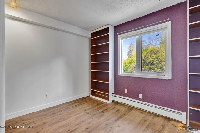 832 O Pl Unit 832, Anchorage, AK 99501 - spare room featuring a baseboard radiator, wood finished floors, baseboards, a textured ceiling, and wallpapered walls