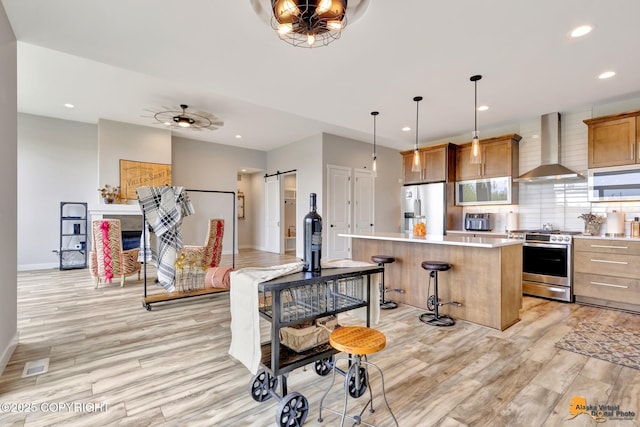 6033 Heather Wood Cir, Anchorage, AK 99502 - kitchen with wall chimney exhaust hood, appliances with stainless steel finishes, a barn door, light wood-type flooring, and a center island