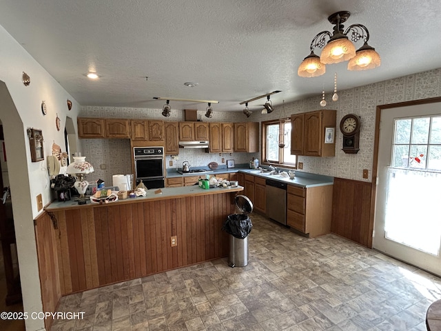 315 On Par Ln, Soldotna, AK 99669 - kitchen with appliances with stainless steel finishes, under cabinet range hood, a peninsula, brown cabinetry, and a wainscoted wall