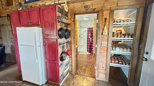 kitchen with freestanding refrigerator, reddish brown cabinets, wood finished floors, and wood walls