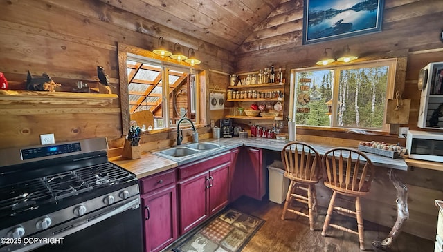 kitchen with stainless steel range with gas stovetop, a sink, vaulted ceiling, wood walls, and dark wood-style flooring
