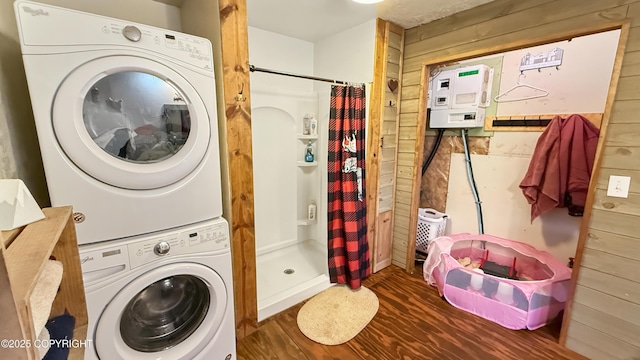 clothes washing area with estacked washer and dryer, wooden walls, and wood finished floors