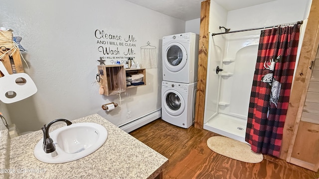 full bathroom with estacked washer and dryer, a baseboard radiator, a shower stall, wood finished floors, and vanity