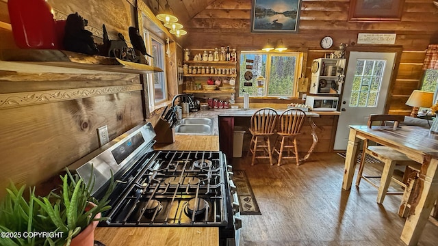 kitchen featuring a sink, stainless steel gas stove, open shelves, wood-type flooring, and white microwave