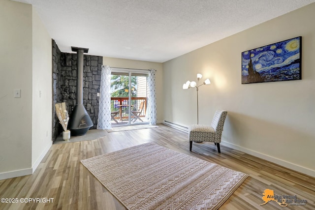 4640 Reka Dr Unit 19, Anchorage, AK 99508 - living area with a wood stove, a baseboard radiator, baseboards, wood finished floors, and a textured ceiling