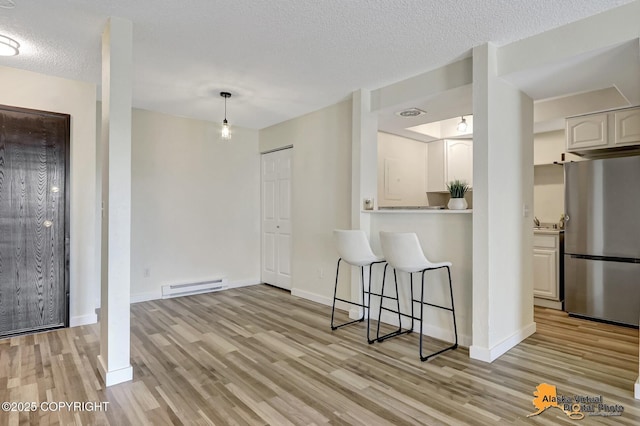 4640 Reka Dr Unit 19, Anchorage, AK 99508 - kitchen featuring freestanding refrigerator, light wood-style floors, a baseboard heating unit, a kitchen breakfast bar, and baseboards