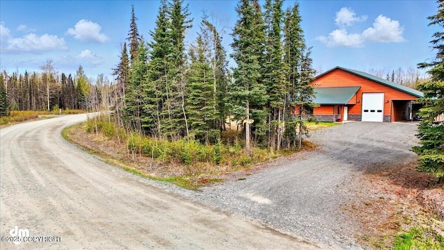 37638 Dutch Landing Loop, Sterling, AK 99672 - view of front of house with dirt driveway, stone siding, a garage, and a view of trees