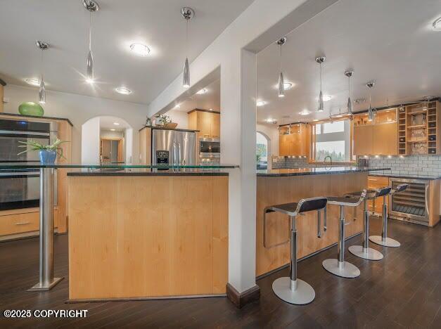 37397 Cetacea Ln, Kenai, AK 99611 - kitchen with stainless steel appliances, dark countertops, arched walkways, decorative backsplash, and dark wood-style flooring