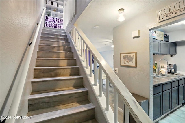 staircase featuring a ceiling fan and a textured wall