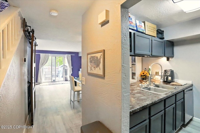 bar area with a sink, stainless steel dishwasher, light wood-type flooring, and a textured wall