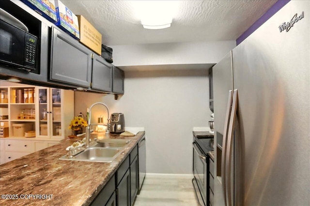 kitchen featuring appliances with stainless steel finishes, a sink, light wood-type flooring, a textured ceiling, and baseboards