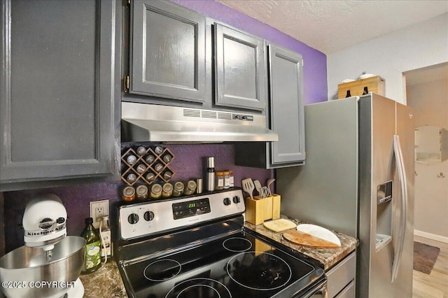 kitchen featuring stainless steel appliances, under cabinet range hood, a textured ceiling, and wood finished floors