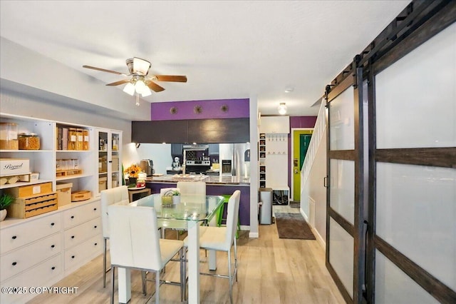dining area featuring a barn door, light wood finished floors, and a ceiling fan