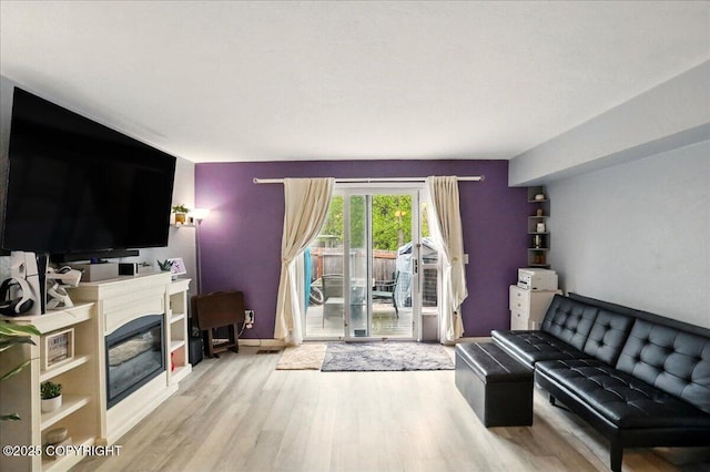 living area featuring wood finished floors, baseboards, and a glass covered fireplace